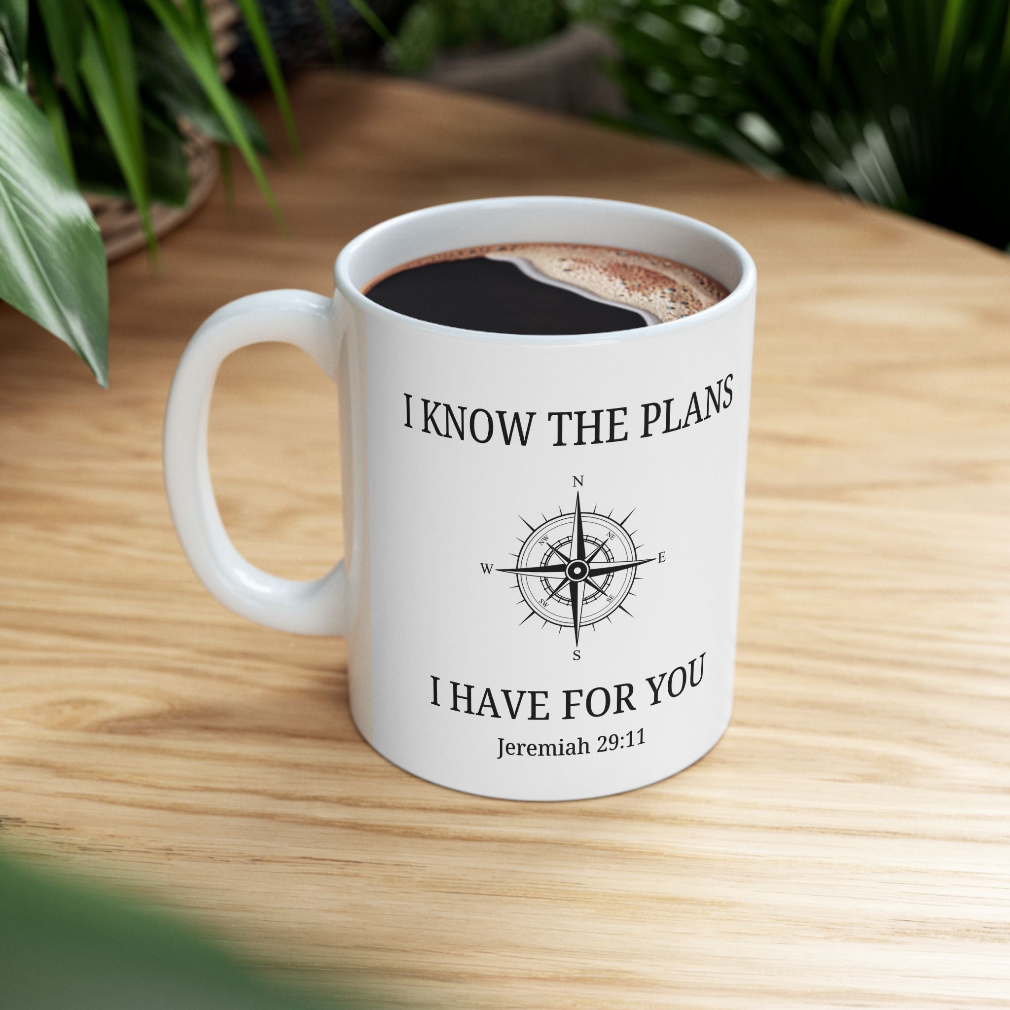 White mug with coffee on a wooden table, featuring a compass design and text.