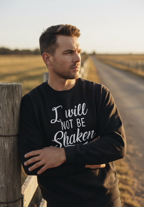 Rugged man leaning on fence wearing I Will Not Be Shaken Psalm 16:8 sweatshirt.